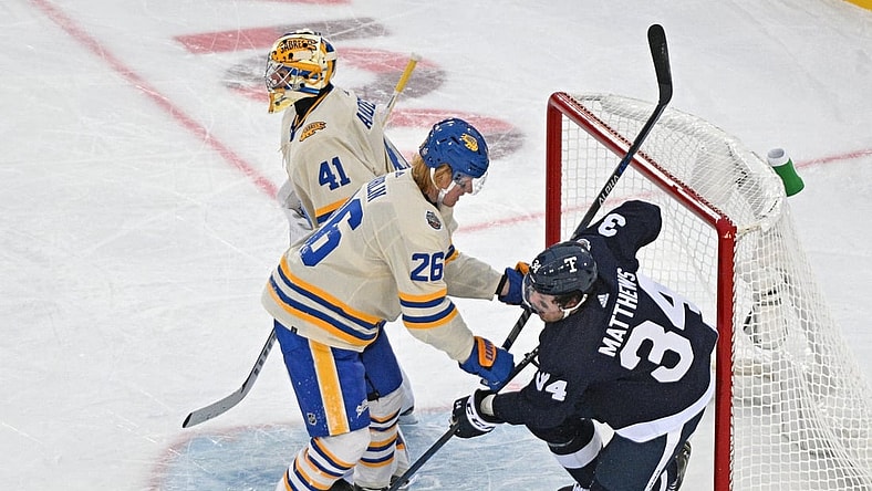 Mar 13, 2022; Hamilton, Ontario, CAN; Buffalo Sabres defenseman Rasmus Dahlin (26) knocks Toronto Maple Leafs forward Auston Matthews (34) into the goal behind goalie Craig Anderson (41) in the 2022 Heritage Classic ice hockey game at Tim Hortons Field. Mandatory Credit: Dan Hamilton-USA TODAY Sports