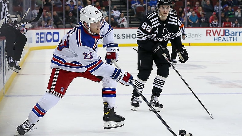 Mar 22, 2022; Newark, New Jersey, USA; New York Rangers defenseman Adam Fox (23) skates with the puck past New Jersey Devils center Jack Hughes (86) during the third period at Prudential Center. Mandatory Credit: Tom Horak-USA TODAY Sports