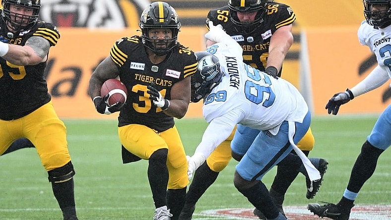 Sep 5, 2022; Hamilton, Ontario, CAN;   Hamilton Tiger-Cats running back Sean Thomas Erlington (31) carries the ball past Toronto Argonauts lineman Dewayne Hendrix (99) in the first half of the annual Labor Day Classic at Tim Hortons Field. Mandatory Credit: Dan Hamilton-USA TODAY Sports