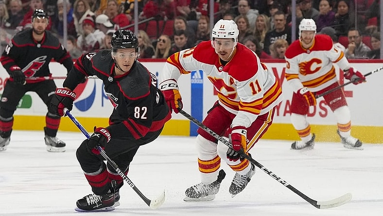 Nov 26, 2022; Raleigh, North Carolina, USA; Carolina Hurricanes center Jesperi Kotkaniemi (82) carries the puck past Calgary Flames center Mikael Backlund (11) during the first period at PNC Arena. Mandatory Credit: James Guillory-USA TODAY Sports