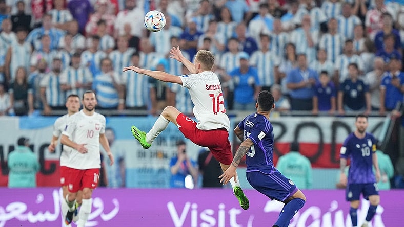 Nov 30, 2022; Doha, Qatar; Poland forward Karol Swiderski (16) leaps for a header past Argentina defender Cristian Romero (13) during the second half in a group stage match during the 2022 World Cup at Stadium 974. Mandatory Credit: Danielle Parhizkaran-USA TODAY Sports