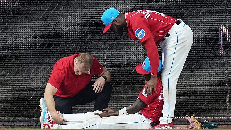 May 13, 2023; Miami, Florida, USA;  Miami Marlins left fielder Bryan De La Cruz (14) holds up center fielder Jazz Chisholm Jr. (2) as he has his leg examined after colliding with the centerfield wall in the eighth inning against the Cincinnati Reds at loanDepot Park. Mandatory Credit: Jim Rassol-USA TODAY Sports