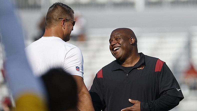 Jul 28, 2023; Ashburn, VA, USA; Washington Commanders assistant head coach/offensive coordinator Eric Bieniemy (R) jokes with Commanders defensive line coach Jeff Zgonina (L) during warmup on day three of Commanders training camp at OrthoVirginia Training Center. Mandatory Credit: Geoff Burke-USA TODAY Sports