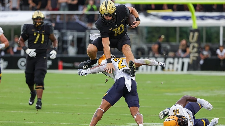 Aug 31, 2023; Orlando, Florida, USA; UCF Knights quarterback John Rhys Plumlee (10) jumps over Kent State Golden Flashes safety Bryce Sheppert (27) during the first quarter at FBC Mortgage Stadium. Mandatory Credit: Mike Watters-USA TODAY Sports battle for the ball