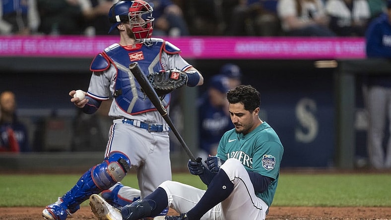 Sep 30, 2023; Seattle, Washington, USA; Seattle Mariners second baseman Josh Rojas (4) sits on the ground after dodging a pitch during the fifth inning at T-Mobile Park. At right is Texas Rangers catcher Jonah Heim (28). Mandatory Credit: Stephen Brashear-USA TODAY Sports