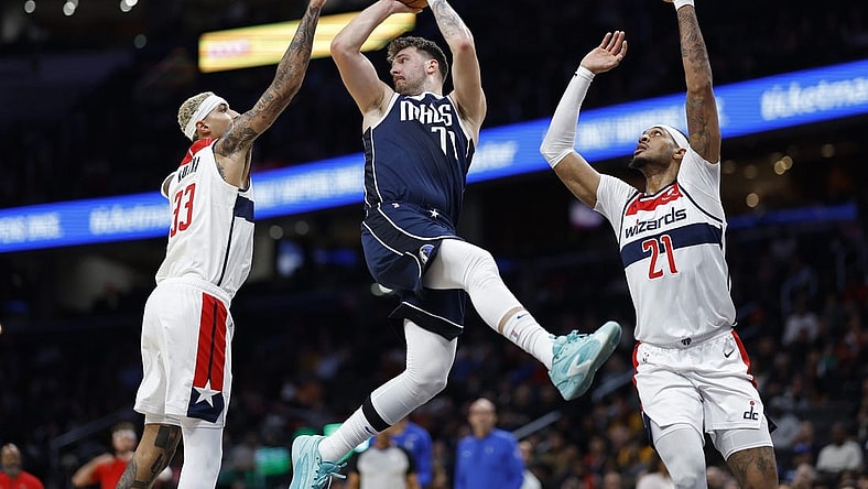 Nov 15, 2023; Washington, District of Columbia, USA; Dallas Mavericks guard Luka Doncic (77) leaps to pass the ball as Washington Wizards forward Kyle Kuzma (33) and Wizards center Daniel Gafford (21) defend in the first quarter at Capital One Arena. Mandatory Credit: Geoff Burke-USA TODAY Sports