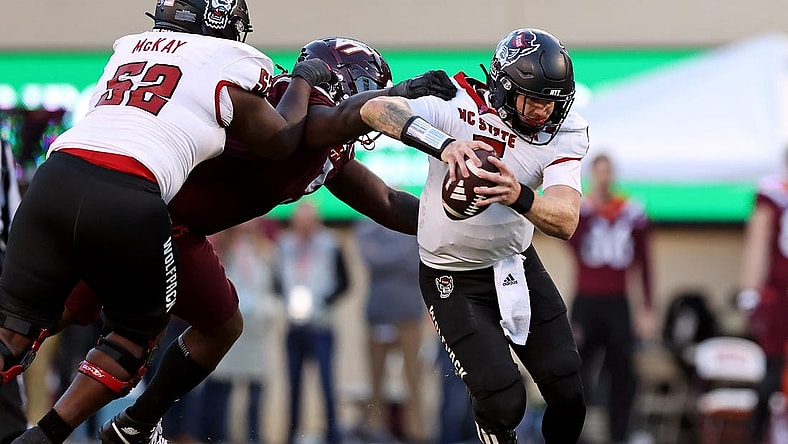 Nov 18, 2023; Blacksburg, Virginia, USA; North Carolina State Wolfpack quarterback Brennan Armstrong (5) runs from Virginia Tech Hokies defensive lineman Norell Pollard (3) during the second quarter at Lane Stadium. Mandatory Credit: Peter Casey-USA TODAY Sports
