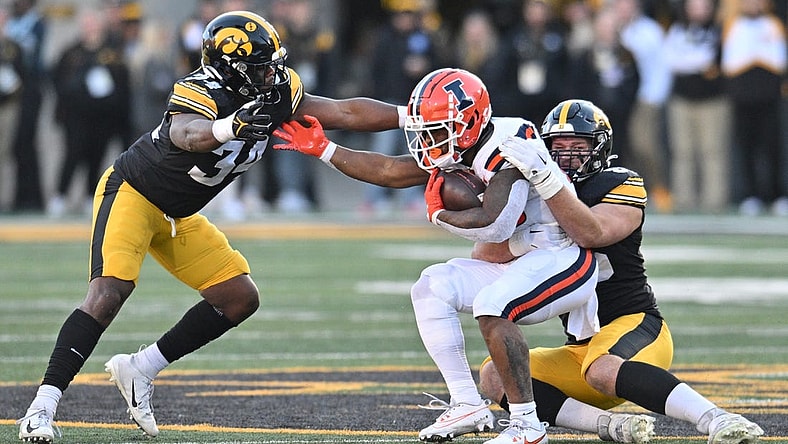 Nov 18, 2023; Iowa City, Iowa, USA; Illinois Fighting Illini running back Reggie Love III (23) is tackled by Iowa Hawkeyes defensive lineman Logan Lee (85) and linebacker Jay Higgins (34) during the second quarter at Kinnick Stadium. Mandatory Credit: Jeffrey Becker-USA TODAY Sports