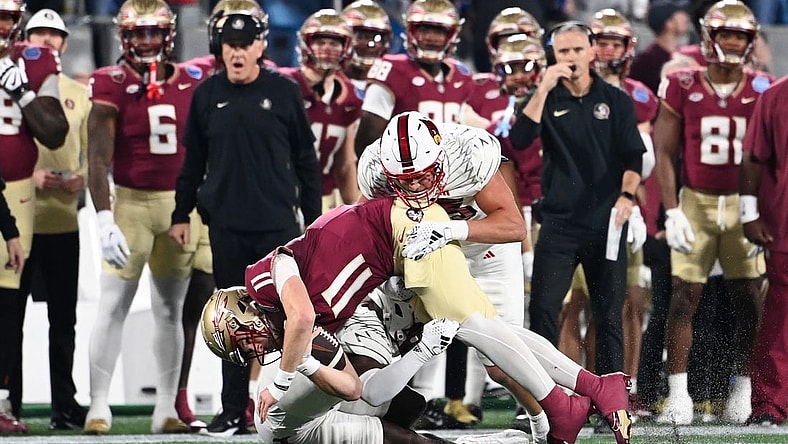 Dec 2, 2023; Charlotte, NC, USA; Florida State Seminoles quarterback Brock Glenn (11) is tackled by Louisville Cardinals defensive lineman Mason Reiger (95) and defensive back Quincy Riley (3) as he runs the ball in the second quarter at Bank of America Stadium. Mandatory Credit: Bob Donnan-USA TODAY Sports