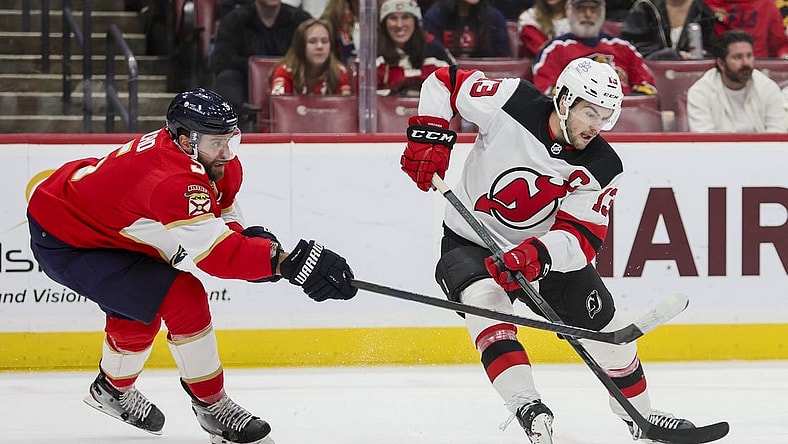 Jan 13, 2024; Sunrise, Florida, USA; New Jersey Devils center Nico Hischier (13) protects the puck from Florida Panthers defenseman Aaron Ekblad (5) during the first period at Amerant Bank Arena. Mandatory Credit: Sam Navarro-USA TODAY Sports