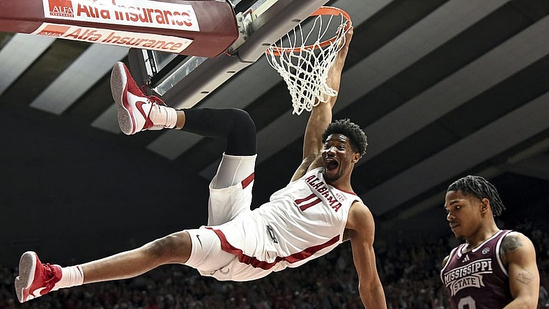 Feb 3, 2024; Tuscaloosa, Alabama, USA;  Alabama forward Mohamed Wague (11) hangs on the rim with a huge smile after dunking over Mississippi State guard Shakeel Moore (3) at Coleman Coliseum. Mandatory Credit: Gary Cosby Jr.-USA TODAY Sports