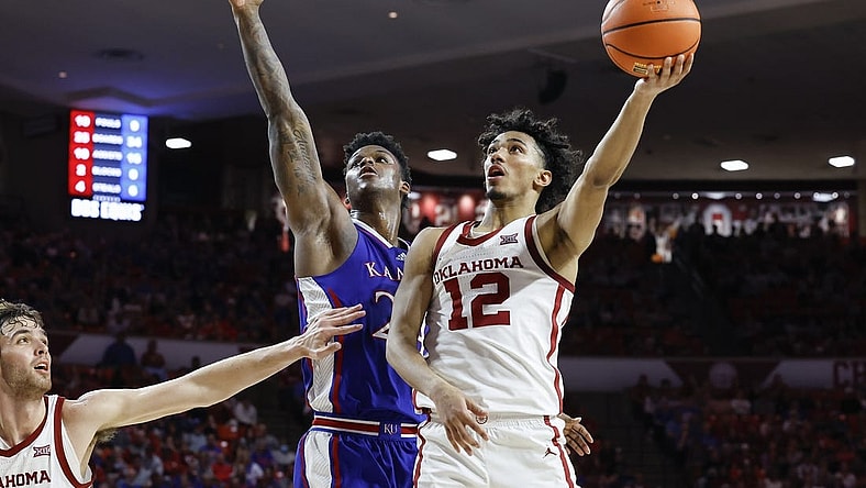 Feb 17, 2024; Norman, Oklahoma, USA; Oklahoma Sooners guard Milos Uzan (12) goes up for a basket beside Kansas Jayhawks forward K.J. Adams Jr. (24) during the second half at Lloyd Noble Center. Mandatory Credit: Alonzo Adams-USA TODAY Sports