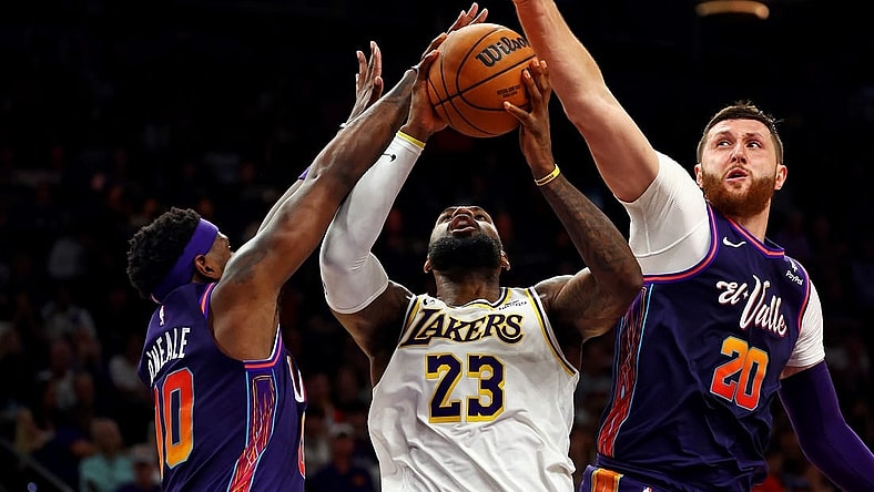 Feb 25, 2024; Phoenix, Arizona, USA; Los Angeles Lakers forward LeBron James (23) shoots the ball against Phoenix Suns forward Royce O'Neale (00) and center Jusuf Nurkic (20) during the fourth quarter at Footprint Center. Mandatory Credit: Mark J. Rebilas-USA TODAY Sports