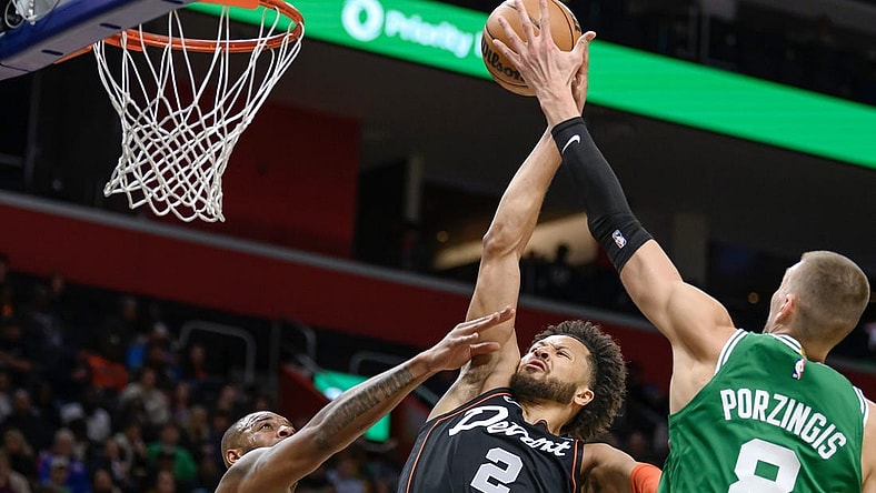 Mar 22, 2024; Detroit, Michigan, USA; Detroit Pistons guard Cade Cunningham (2) gets fouled while driving to the basket against  Boston Celtics forward Xavier Tillman (26) and  center Kristaps Porzingis (8) in the first quarter at Little Caesars Arena. Mandatory Credit: Lon Horwedel-USA TODAY Sports